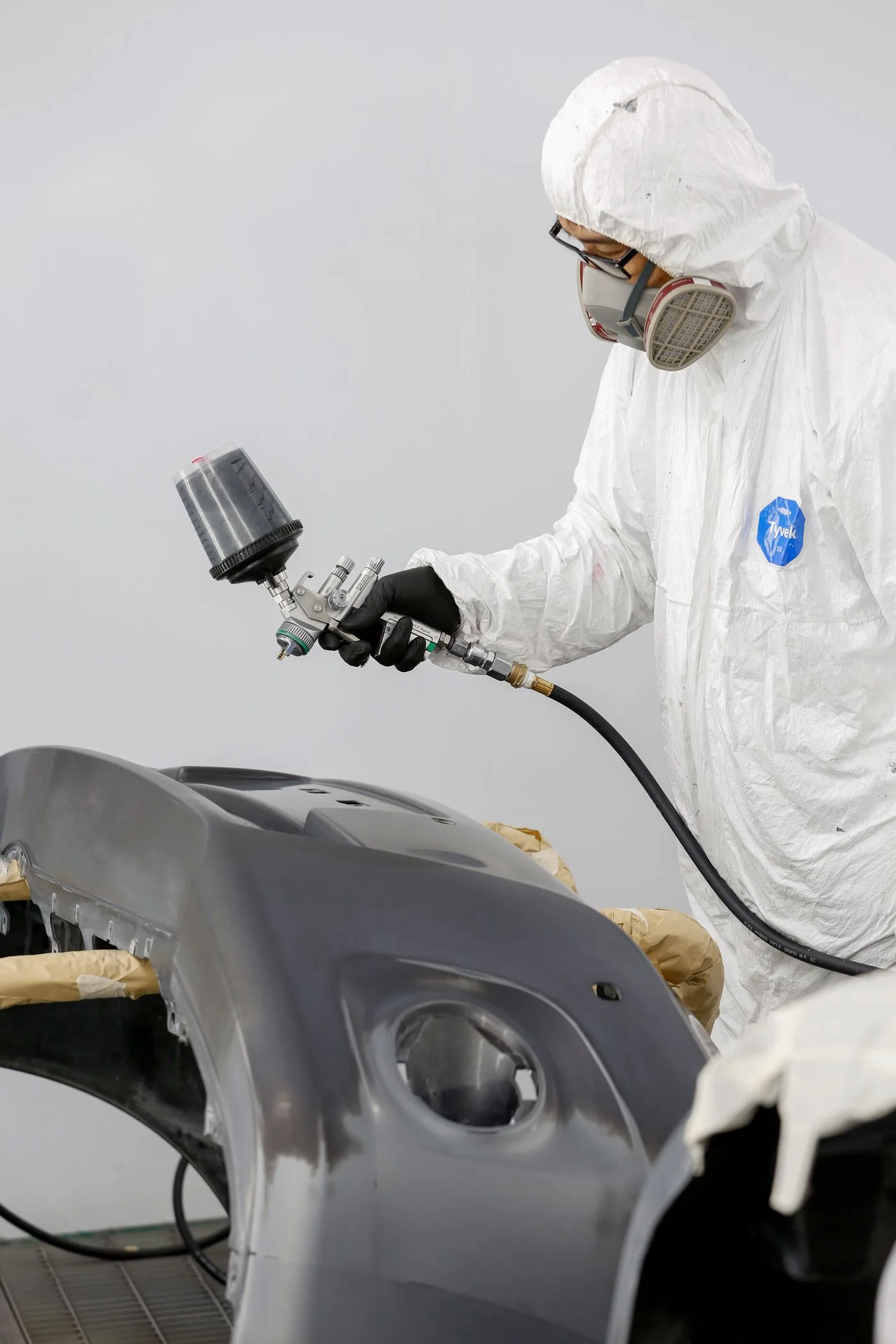 Painter in a spray booth refinishing a bumper cover with an HVLP spray gun